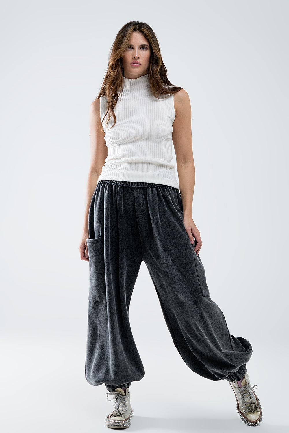 Sleeveless high neck wool jumper in white worn with loose black velvet trousers and trainers