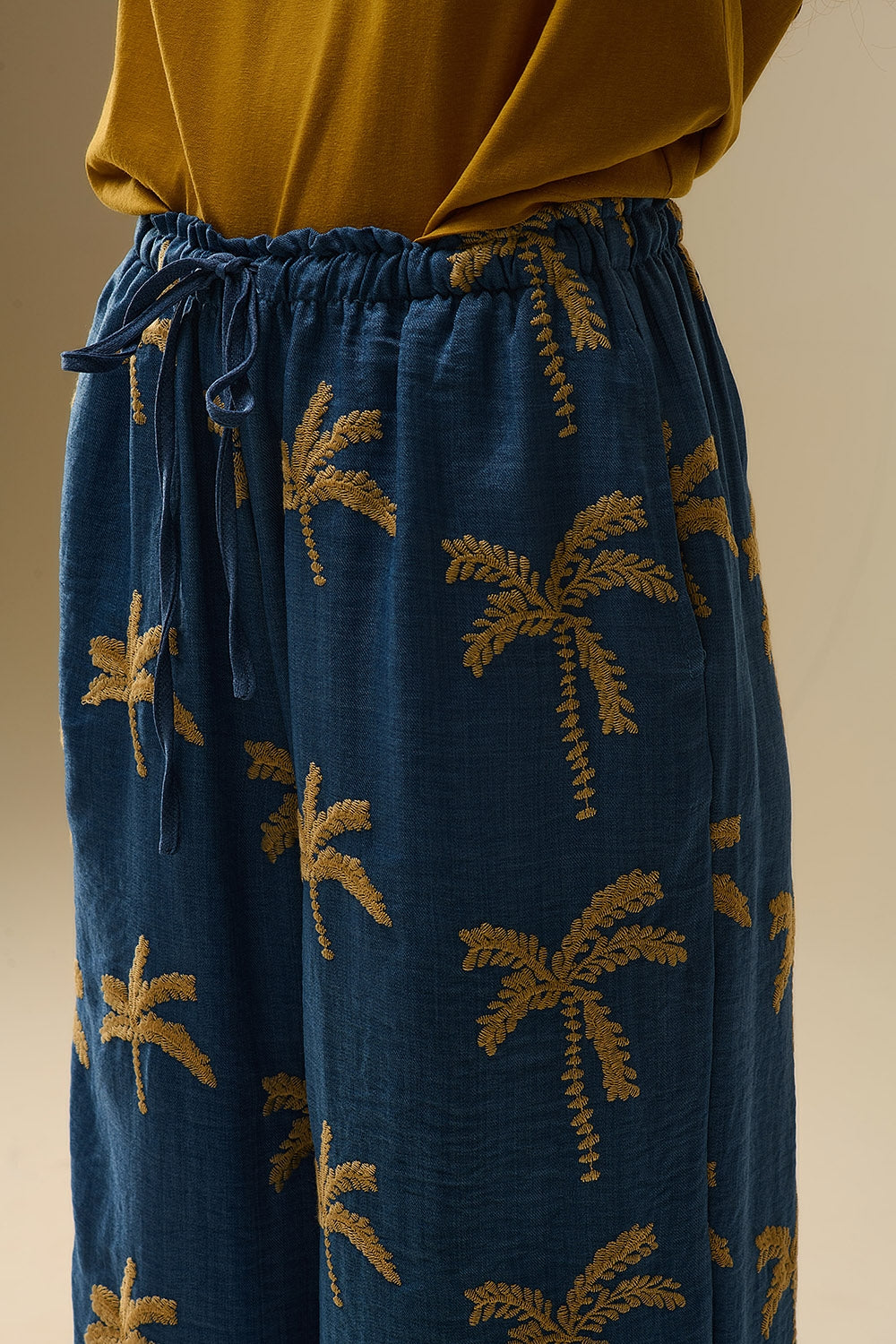 Calça de perna larga azul com bordado de palmeira bege