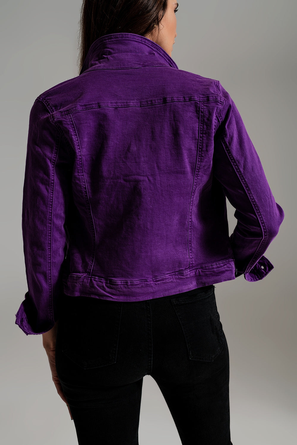 Back view of fitted purple jean jacket worn by woman with black jeans