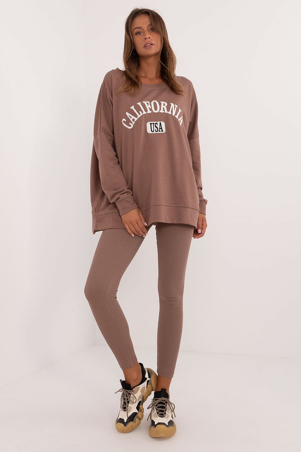 Woman wearing a brown oversized sweatshirt and leggings set with California USA print and sneakers