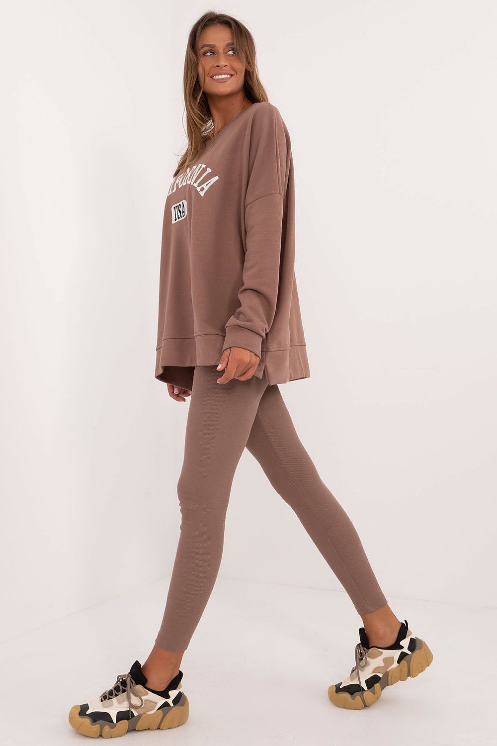 Woman wearing brown oversized sweatshirt and leggings set paired with beige and black sneakers