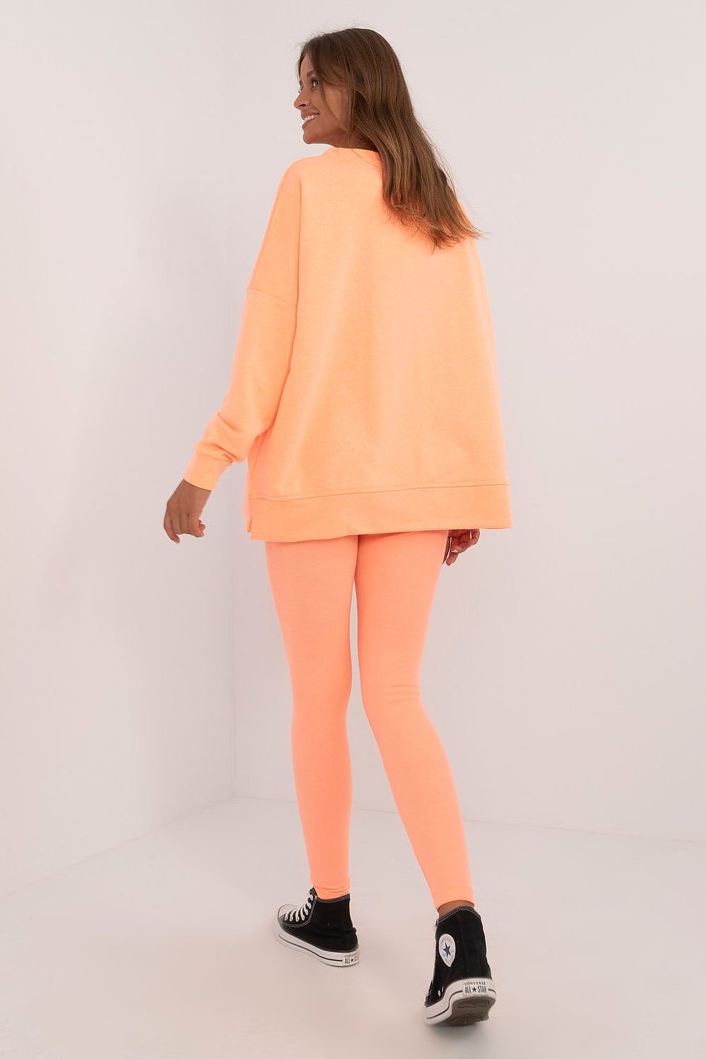 Woman wearing a peach oversized sweatshirt and leggings set from Factory Price, paired with black high-top sneakers